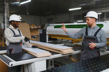 İki marangoz, bir mobilya fabrikasının yanında ahşap işlemeyi tartışıyor, kalite kontrol ve üretim verimliliği konusunda işbirliği yapıyorlar.