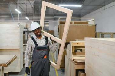 Ahşap çerçeve taşıyan, ahşap ve makinelerle çevrili bir mobilya fabrikasında çalışan kendinden emin bir marangoz.