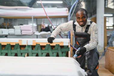 Marangoz bir mobilya fabrikasında kanepe monte ediyor, ahşap iskeleti sağlamlaştırmak için pnömatik zımba tabancasını ustalıkla kullanıyor.