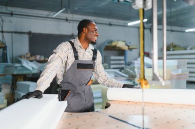 Afrikalı Amerikalı işçiler bir mobilya fabrikasında cnc makinesini ustalıkla yönetiyor, sanayi ortamında kanepe üretimi için malzeme hazırlıyorlar.
