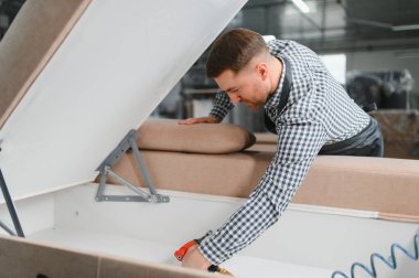 Marangoz bir mobilya fabrikasında kanepe monte ediyor. Üretim sürecinde hassasiyet ve kaliteyi sağlamak için pnömatik zımba kullanıyor.