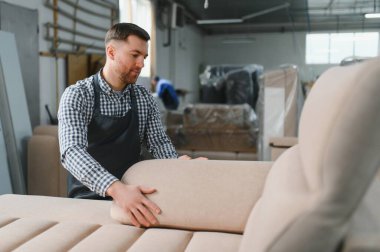 Marangoz bir mobilya fabrikasında çalışıyor, bir kanepeyi döşüyor, dikişlerin ve kumaşın kalitesini kontrol ediyor.