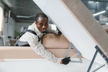 Mobilyacı, mobilya fabrikasında şık bir kanepeyi monte ederken cıvataları sıkıyor, marifetli işçilik ve hassasiyet sergiliyor.