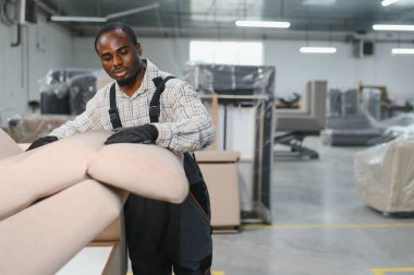 Bir kanepe yapmaya odaklanan Afro-Amerikan bir zanaatkar, hareketli bir mobilya fabrikasında döşemeleri ustalıkla birleştiriyor.