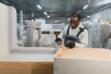 Marangoz mobilya parçalarını kartonla güzelce paketliyor. Mobilya fabrikası içinde güvenli nakliye için.