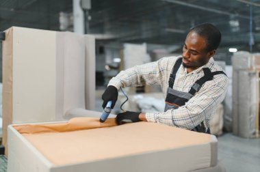 Mobilya fabrikasında pnömatik zımba tabancası kullanarak kanepe çerçevesine kumaş geren ve tamir eden konsantre Afro-Amerikan bir zanaatkar.