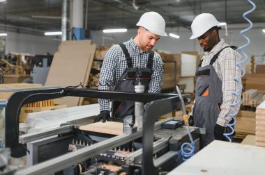 İki marangoz bir mobilya fabrikasında cnc makinesi çalıştırıyor, kanepeler için ahşap parçalar üretiyor.