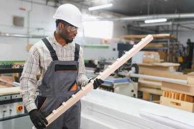 Marangoz, mobilya fabrikasındaki tahtalarla ahşap bir kalası inceliyor. Üretim sürecinde kalite ve hassasiyet sağlıyor.