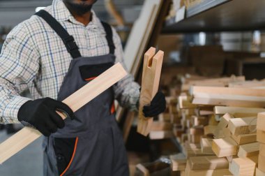 Marangoz eldiven takıyor, mobilya fabrikasında iki ahşap kalası karşılaştırıyor, ahşap işçiliğinde kalite ve hassasiyet sağlıyor.