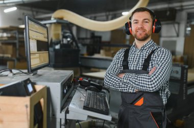 Marangoz, bir mobilya fabrikasında, işitme koruması ve tulum giyiyor.