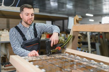 Marangoz, hareketli bir mobilya fabrikasında ahşap bir kanepe çerçevesi monte ederken pnömatik bir zımba tabancası kullanıyordu.