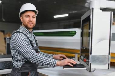 Marangoz bir mobilya fabrikasında bir cnc makinesini kontrol ediyor, üretimde kalite ve kesinlik sağlıyor.