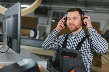 Mobilya fabrikasında çalışan bir işçi hassas ahşap kesme makinesi kullanıyor. Koruyucu giysiler giyip, verimli kanepe üretimine odaklanmış.