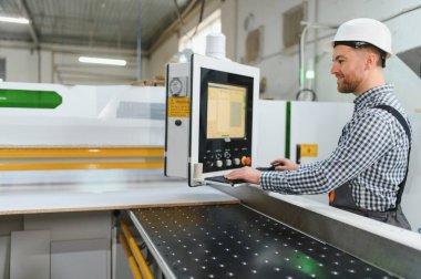 Mobilya fabrikasında güvenlik kaskı takan marangoz, bilgisayar sayısal kontrol sistemiyle süreci kontrol ediyor.