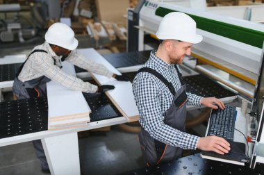 İki farklı fabrika işçisi bir cnc makinesi kullanıyor, mobilya parçaları üretiyorlar, takım çalışması ve modern üretim süreçlerini sergiliyorlar.
