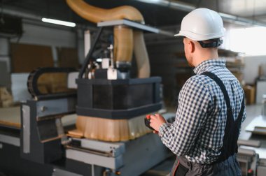 Mobilya fabrikasında çalışan bir işçi, ahşap malzemelerle çevrili, kanepe üretimindeki hassasiyet ve verimliliğe odaklanan bir cnc makinesi kullanıyor.