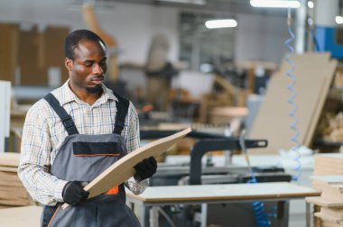 Yetenekli marangoz yoğun bir mobilya fabrikasında kalite ve hassasiyet sağlamak için bir parça ahşabı dikkatlice inceliyor.
