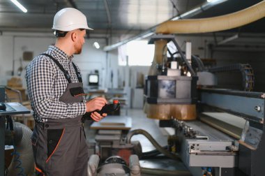 Marangoz uzaktan kumandayla bir cnc makinesini kontrol ediyor, modern bir marangoz fabrikasında mobilya parçaları üretiyor.