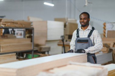 Marangoz, kaliteli işçiliğe odaklanmış, hareketli bir mobilya fabrikasında çalışırken ahşap bir kalası ustalıkla tutuyor.