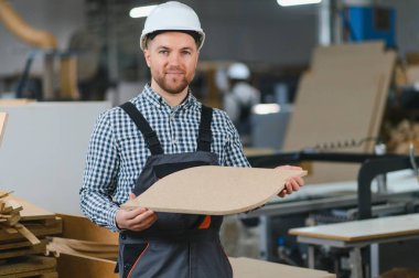 Marangoz, bir mobilya fabrikasında cnc makinesi tarafından üretilen bir tahta parçasını gösteriyor.