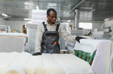 Mobilyacı, hareketli bir fabrikada kanepe monte ediyor, marifetli bir işçilik sergiliyor ve üretim sürecindeki detaylara dikkat ediyor.