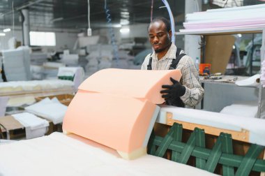 Mobilyacı döşeme atölyesinde bir kanepe kuruyor, kaliteli işçilik yaratmak için köpük ve ahşapla ustalıkla çalışıyor.