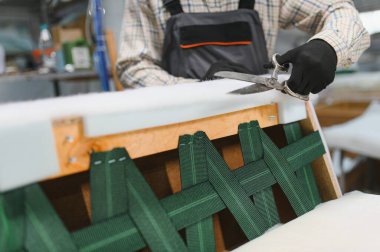 Mobilya fabrikasında çalışan bir zanaatkar kanepe yaparken fazla kumaşı makasla kesiyor.