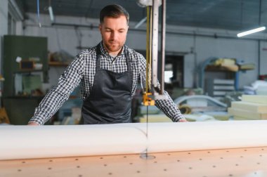 Marangoz bir mobilya fabrikasında özenle çalışıyor, elektrikli testereyle kumaş kesiyor.