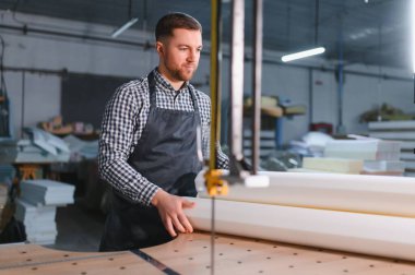 Elektrikli testereyle çalışan marangoz mobilya fabrikasında kanepe üretimi için köpük kesiyor.