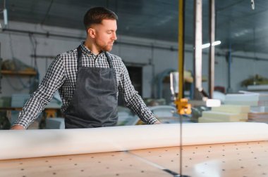 Marangoz atölyede mobilya üretimi için malzeme hazırlarken tezgahın üzerine büyük beyaz kumaş rulosu açıyor.