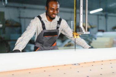 Marangoz elektrikli testereyi ustalıkla kullanıyor, mobilya fabrikasında beyaz kumaş rulosunu kesiyor.