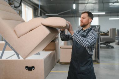 Marangoz bir mobilya fabrikasında kanepe monte ediyor, zanaat sanatını sergiliyor ve küçük işletme üretiminin ithafını sergiliyor.