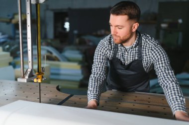 Marangoz, yoğun bir atölyede mobilya döşemesi için beyaz kumaş kesmek için dikey testereyi dikkatlice kullanır.