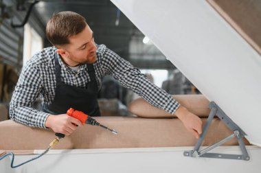 Marangoz, bir mobilya fabrikasında pnömatik tornavidayla kanepe monte ediyor. Yetenekli işçilik ve hassasiyet sergiliyor.