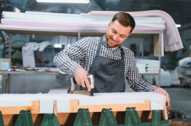 Gülümseyen marangoz, havalı zımba tabancasıyla mobilya fabrikasında kanepe döşeyip marangozluk yeteneklerini sergiliyor.