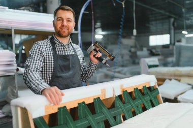 Marangoz pnömatik zımba tabancası kullanıyor, hareketli bir mobilya fabrikasında ustalıkla kanepe üretiminde çalışıyor, kaliteli döşemeler yapıyor.