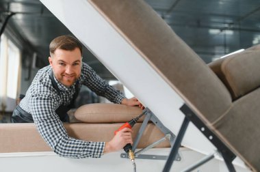 Marangoz, bir mobilya fabrikasında pnömatik tornavida kullanarak bir kanepeyi titizlikle monte ediyor. Yetenekli işçilik ve adanmışlık sergiliyor.