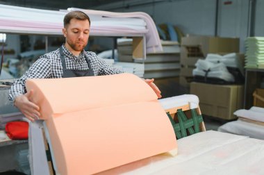 Marangoz mobilya fabrikasında çalışırken koltuğun üzerine dikkatlice köpük kauçuk yerleştiriyor, marangozluk ve detaylara özen gösteriyor.