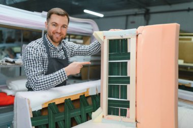 Fabrika işçisi, ahşap ve kumaş bileşenleri, işçilik ve üretim teknikleri üzerine odaklanarak kanepe çerçevesi montaj sürecini sergiliyor.