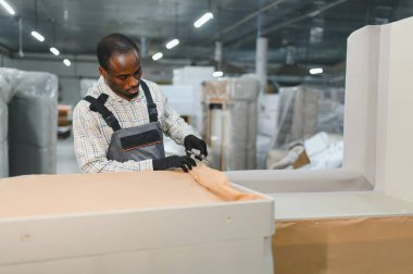 Mobilyacı, hareketli bir fabrikada kanepe döşemesi için kumaş kesiyor, marifetli bir işçilik sergiliyor ve detaylara dikkat ediyor.