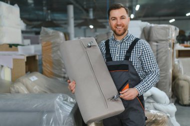 Bir mobilya fabrikasında koltuk parçası tutan gülümseyen bir zanaatkar, kalitesini ve işçiliğini sergiliyor.