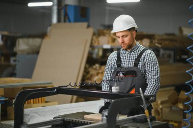 Mobilya fabrikasında çalışan bir işçi hassas ahşap kesme üzerine odaklanan bir makine kullanıyor. Kanepe üretimi için, endüstriyel işçilik sergiliyor.