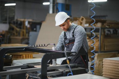 Bir mobilya fabrikasında güvenlik kaskı takan marangoz, mobilyalar ve diğer mobilyalar için ahşap parçalar üretiyor.