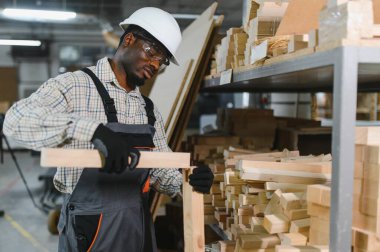 Mobilya fabrikasında ahşap kalasları inceleyen marangoz, üretim sürecinde kalite ve hassasiyet sağlıyor.