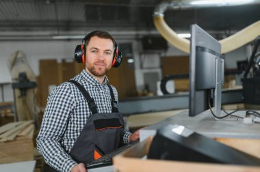 Modern bir mobilya fabrikasında, kulak koruyucu takan marangoz gelişmiş üretim süreçlerini sergiliyor.