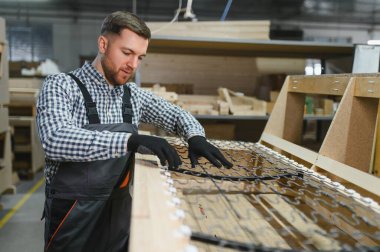 Marangoz, mobilya fabrikasında yaylı ve ahşaplı bir kanepe çerçevesi monte ediyor. Yetenekli işçiliği iş başında sergiliyor.