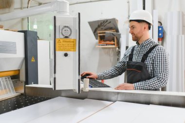 Mobilya fabrikasında güvenlik kaskı takan marangoz, bilgisayar aracılığıyla süreci kontrol ediyor.