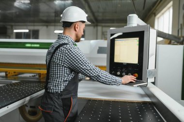 Bir mobilya fabrikasında güvenlik kaskı takan marangoz, mobilyalar ve diğer mobilyalar için ahşap parçalar üretiyor.