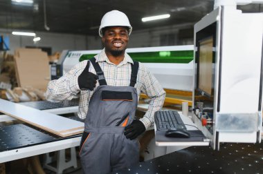 Marangoz, modern marangozluk endüstrisinde bir mobilya fabrikasında cnc makinesi kullanırken başparmağını kaldırıyor.