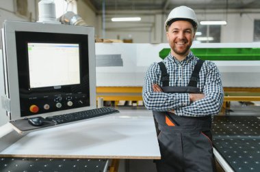 Mobilya fabrikasında kolları çaprazlanmış bir şekilde gülümseyen bir marangoz portresi.